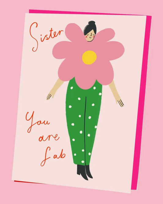 Greeting card with a stylised illustration of a person wearing a large pink flower on a pink background and the words Sister You Are Fab