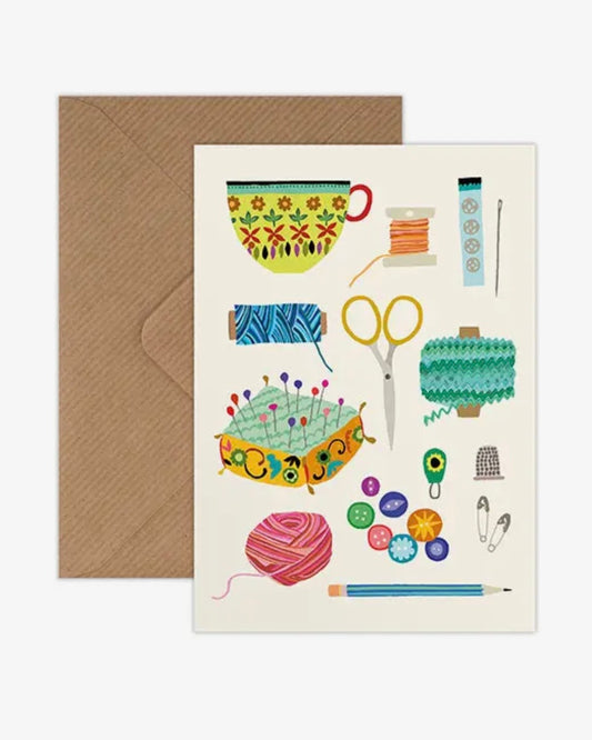 Greeting card with sewing & knitting-themed illustrations and a brown envelope on a white background